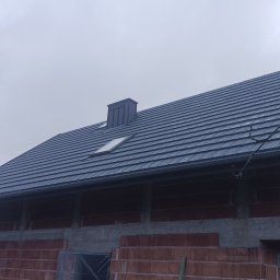 JT BUD - Szary dach z dachówki ceramicznej na budynku w trakcie budowy, widoczne okno dachowe i komin wentylacyjny.