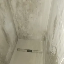 Wnętrze kabiny prysznicowej z odpływem liniowym w posadzce i przygotowanymi przyłączami wodnymi na ścianie, wykończonej płytkami imitującymi beton.