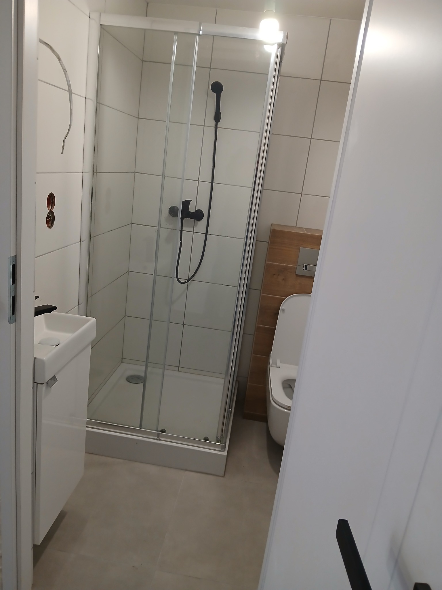 Nowoczesna łazienka z kabiną prysznicową z przezroczystego szkła, białą umywalką z szafką, toaletą z deską sedesową i beżowymi płytkami na ścianach i podłodze.