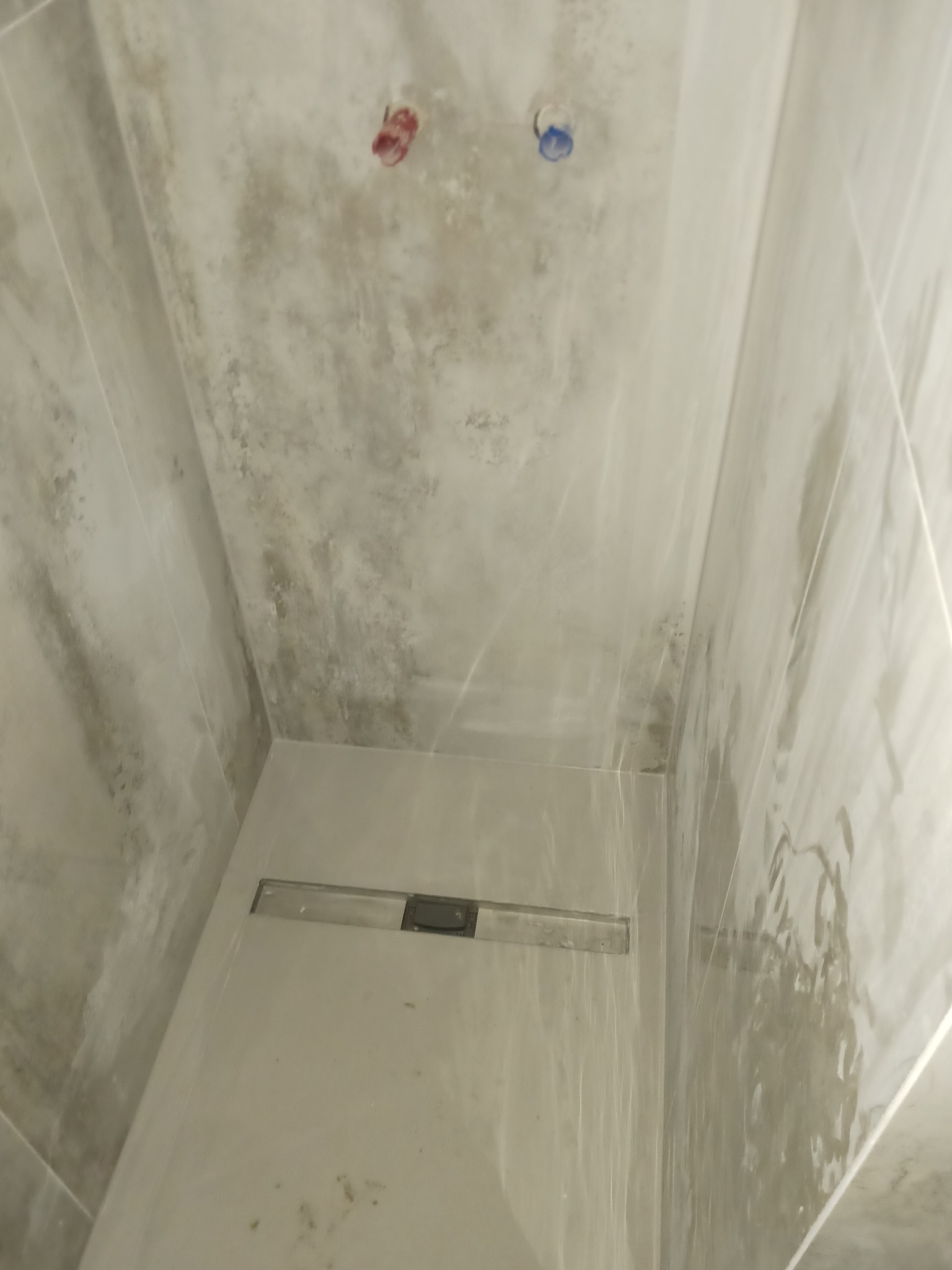 Wnętrze kabiny prysznicowej z odpływem liniowym w posadzce i przygotowanymi przyłączami wodnymi na ścianie, wykończonej płytkami imitującymi beton.