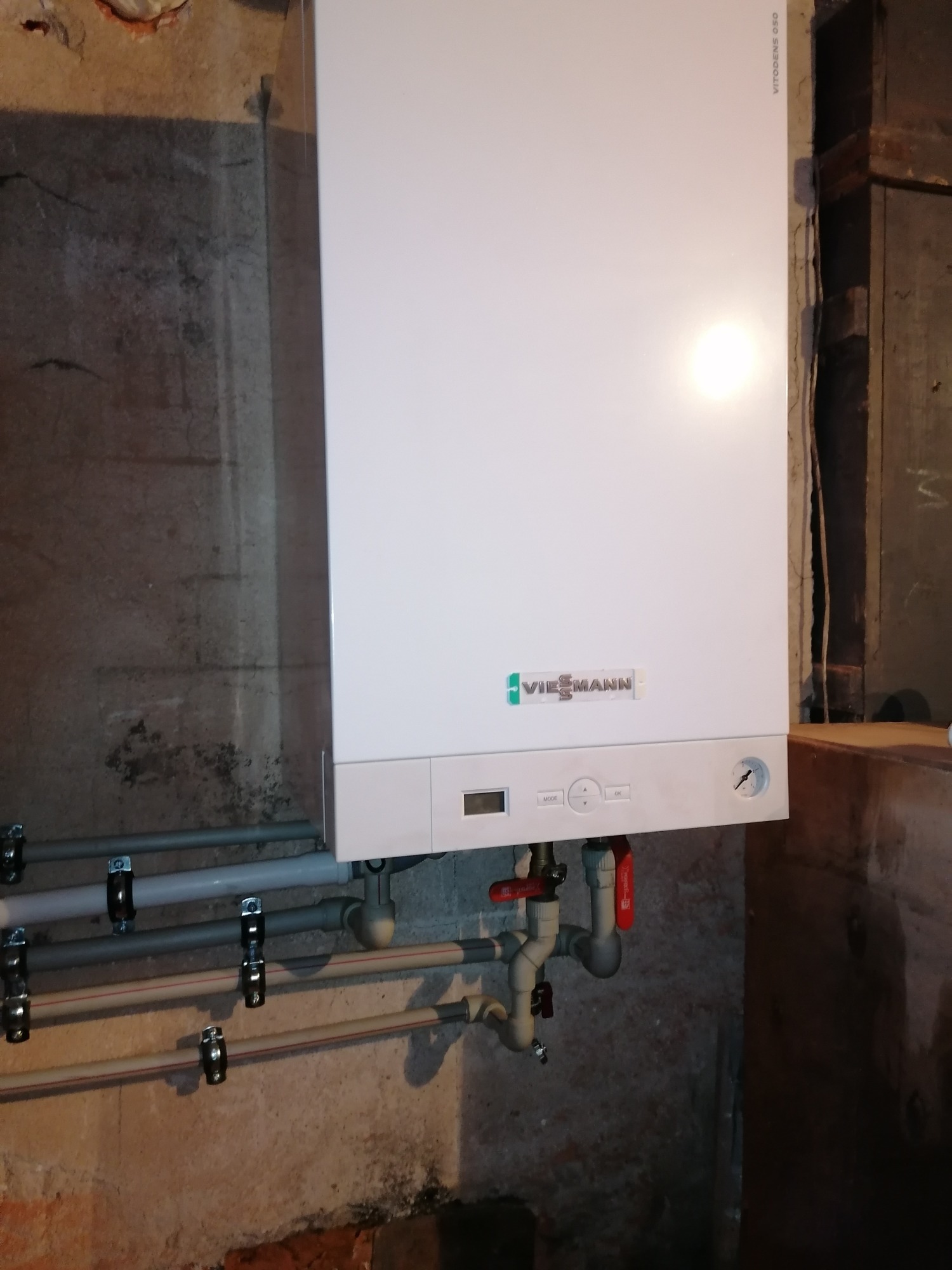 Biały piec gazowy Viessmann Vitodens 050 zamontowany na ścianie z rurami i zaworami, widoczne elementy instalacji grzewczej i gazowej.