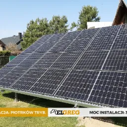 Panel fotowoltaiczny o mocy 3,84 kWp zamontowany na trawie przed domem jednorodzinnym w słoneczny dzień, widoczne elementy konstrukcyjne i logo firmy.