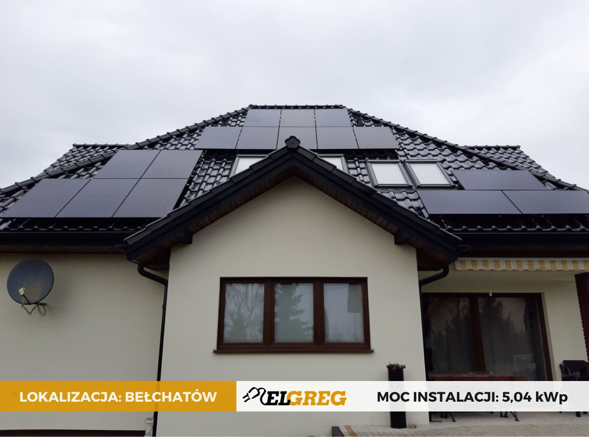 Dom jednorodzinny z zamontowanymi panelami fotowoltaicznymi na dachu z dachówki ceramicznej; widoczne okna dachowe i antena satelitarna na elewacji; w dolnej części kadru informacja o lokalizacji...