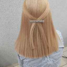 Blond włosy upięte spinką z cyrkoniami, widok z tyłu na tle szarej ściany i kafelkowej podłogi, kobieta w bluzce w niebieskie paski.