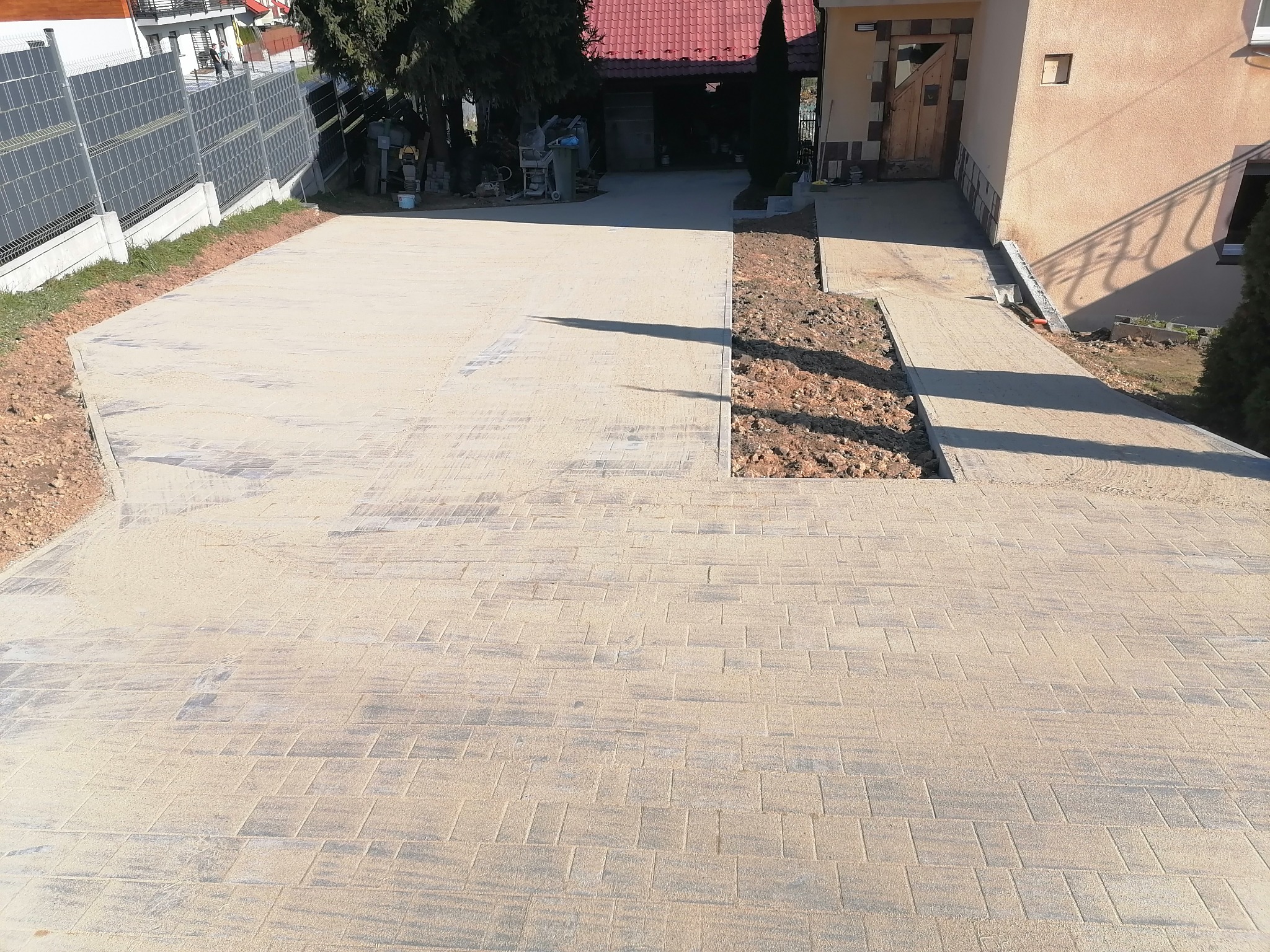 Nowo ułożona, jasna kostka brukowa na podjeździe, z widocznym wykopem pod obrzeża i fragmentem budynku w tle.