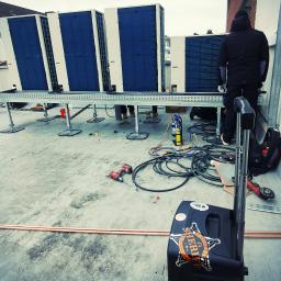 Air Camaro Sp. z o.o. - Instalacja czterech klimatyzatorów na dachu budynku, widoczny monter w czarnej kurtce, narzędzia pracy, przewody i butla z gazem.