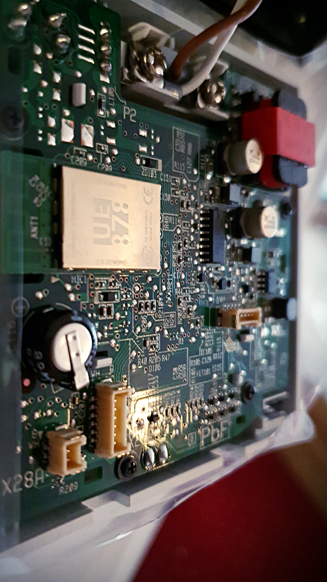 Zbliżenie na zieloną płytkę drukowaną z licznymi elementami elektronicznymi, widoczne złącza, kondensatory, rezystory i układy scalone, detale lutowania.