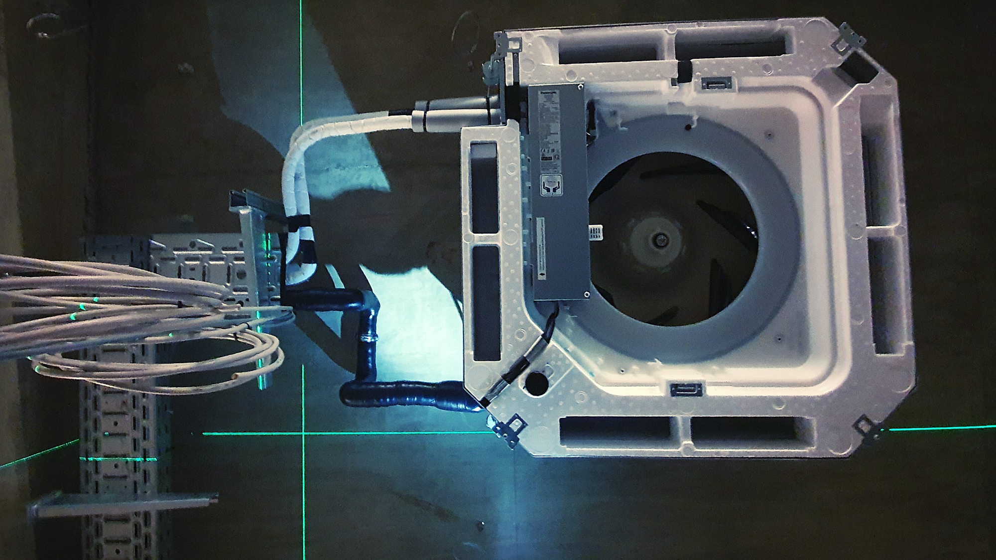 Widok od spodu na zamontowaną jednostkę wewnętrzną klimatyzacji z podłączonymi przewodami, widoczna poziomica laserowa.