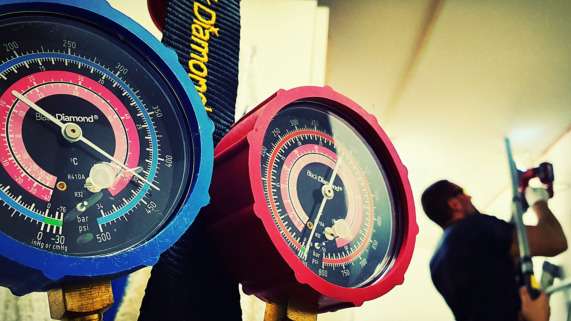 Mierniki ciśnienia chłodniczego Black Diamond z podziałką w stopniach Celsjusza i PSI, widoczne podczas pracy instalatora w białych rękawicach, który montuje element w suficie