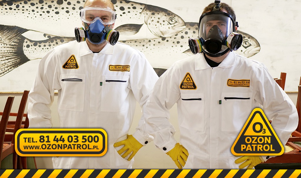 Dwóch pracowników Ozon Patrol w Lublinie, w białych kombinezonach i maskach ochronnych, prezentuje się na tle ściany z rysunkiem ryb.