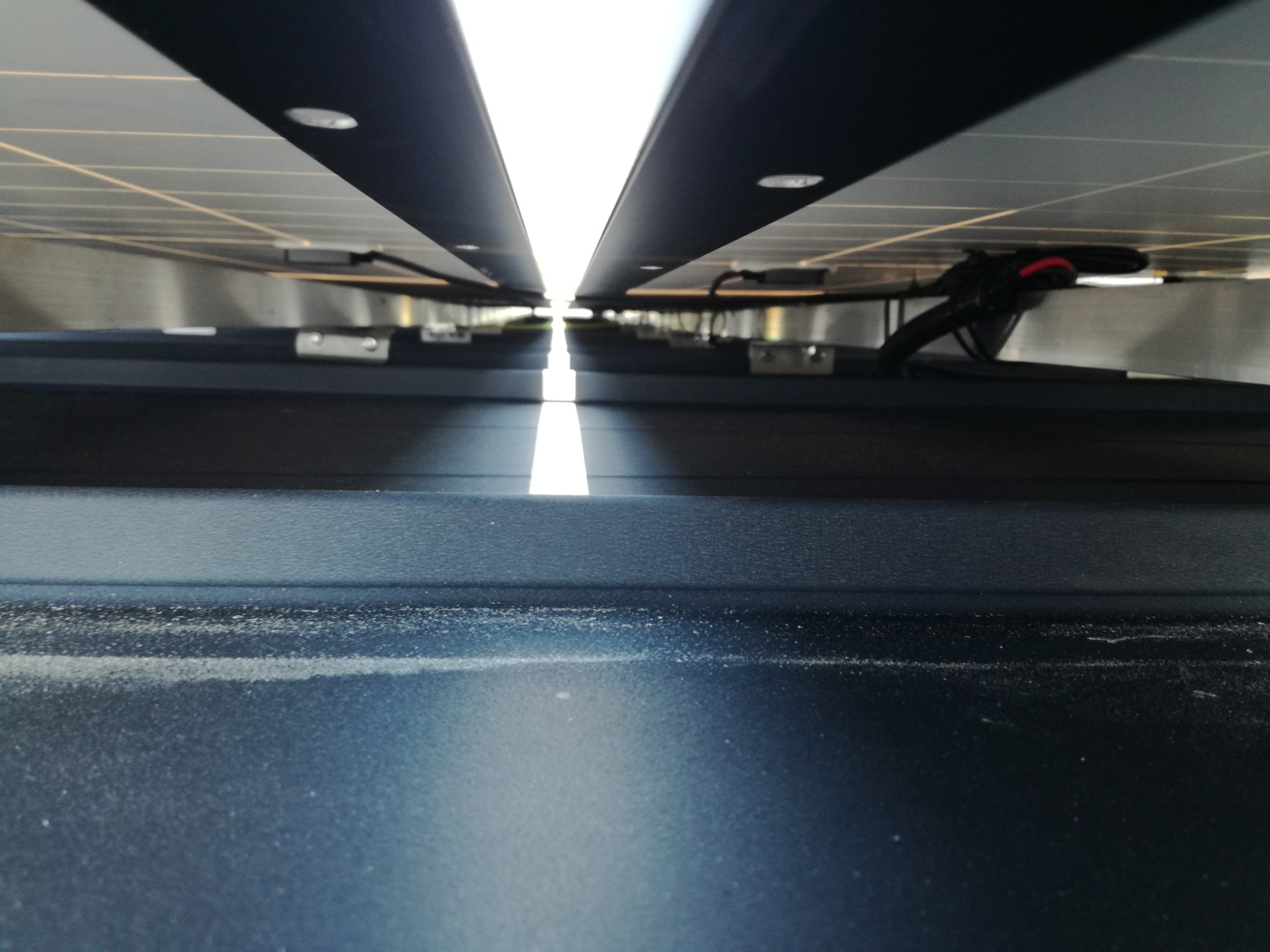 Nietypowe ujęcie od dołu instalacji paneli słonecznych w Lublinie, widoczne mocowania i okablowanie, z jasnym prześwitem na końcu rzędu.