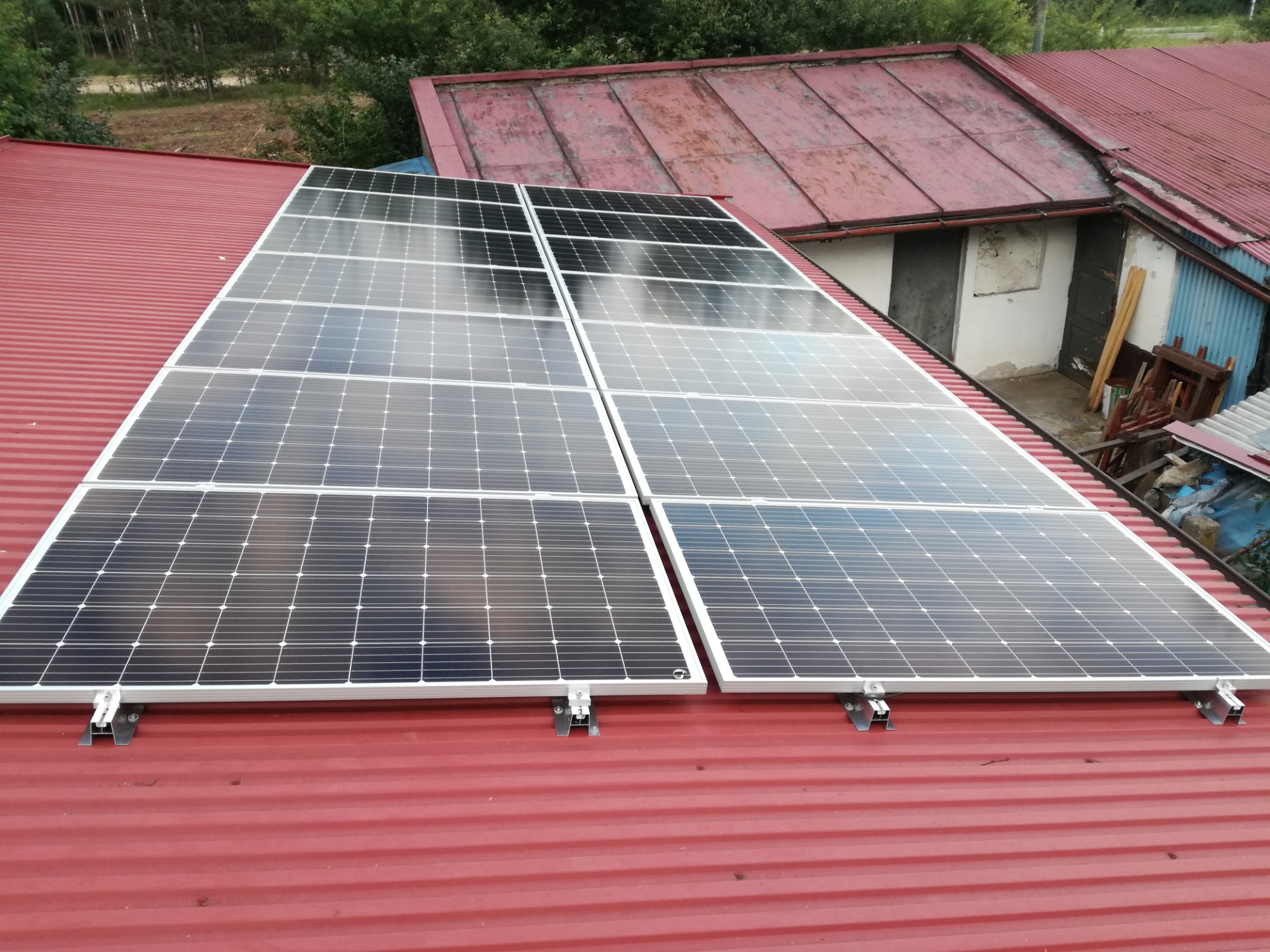 Cztery panele słoneczne zamontowane na czerwonym, blaszanym dachu budynku z widocznymi mocowaniami.