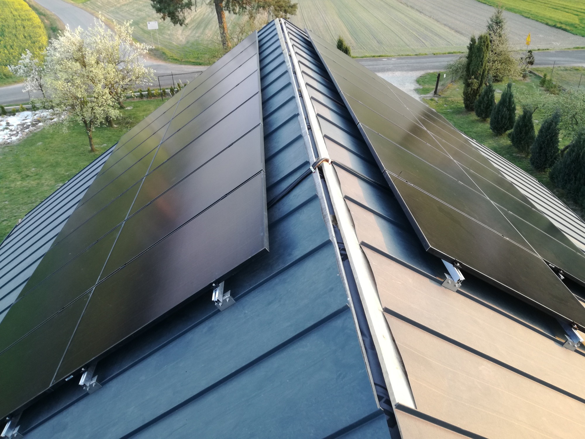 Widok z góry na panele słoneczne na dachu domu z blachy trapezowej, z widocznym krajobrazem w tle.