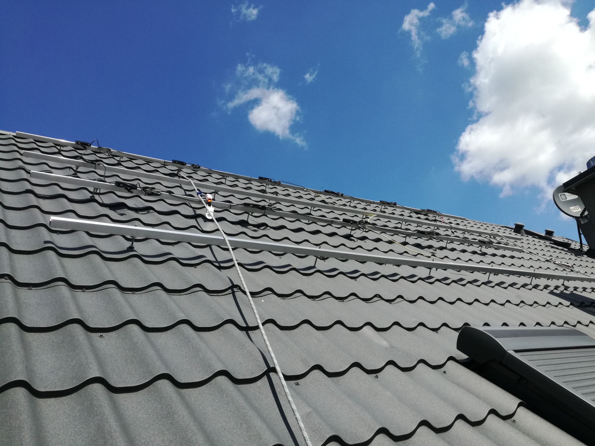 Montaż szyn pod panele na dachu z blachodachówki w słoneczny dzień. Widoczne kable i uchwyty montażowe.