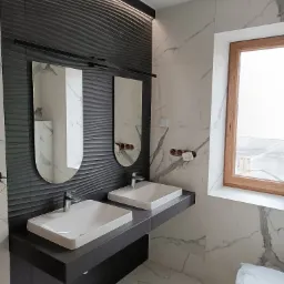 Nowoczesna łazienka w Zagrodach z dwoma umywalkami nablatowymi na ciemnoszarym blacie, podwieszane lustra na tle dekoracyjnej ściany z efektem fal i marmurowe płytki na ścianach i podłodze.