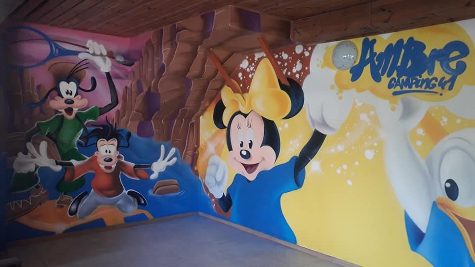Wielkoformatowy mural w pokoju z postaciami z kreskówek Disneya: Goofy, Max, Myszka Minnie, Kaczor Donald, z napisem 'Ambre Camping 41' w prawym górnym rogu.