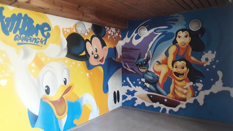 Wnętrze pokoju z muralem przedstawiającym Donalda, Mickey Mouse'a i postacie z Lilo i Stich, wykonanym w jasnych, żywych kolorach.