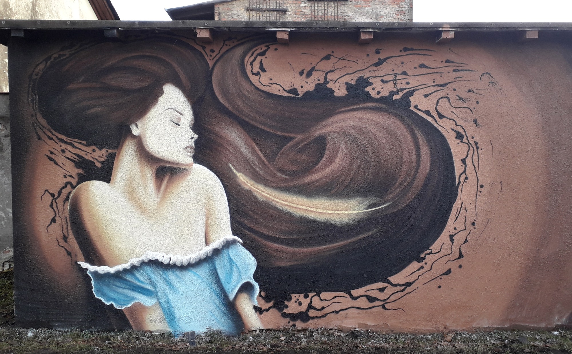 Mural przedstawiający kobietę z rozwianymi brązowymi włosami i w błękitnej sukience na ścianie budynku.