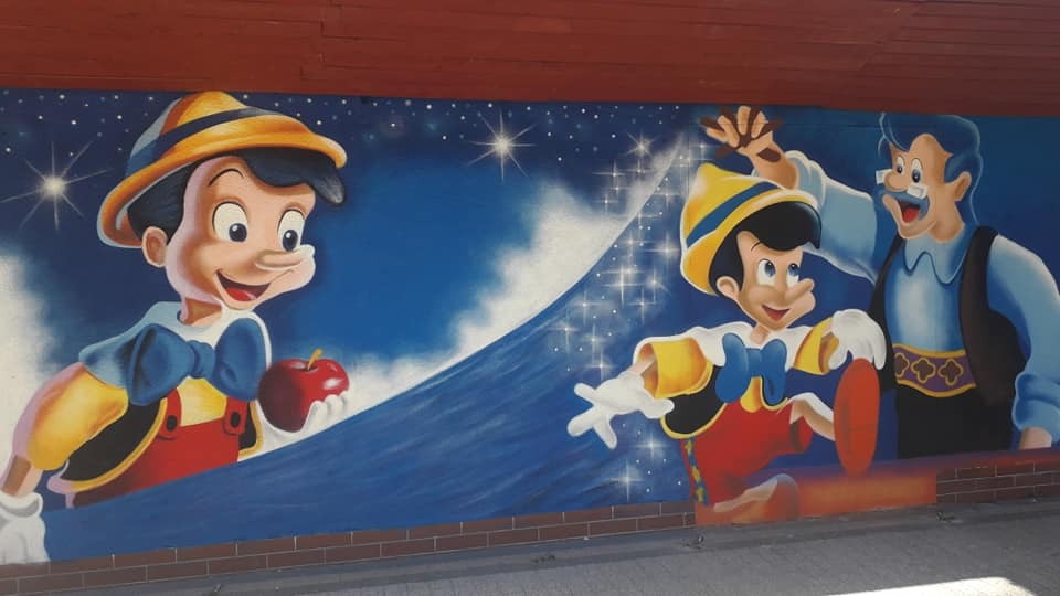 Mural przedstawiający Pinokia i Dżepetto na niebieskim tle z gwiazdami, namalowany na ceglanej ścianie.