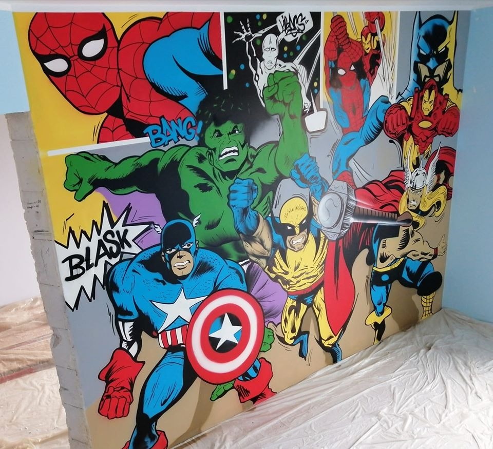 Ściana pokoju z ręcznie malowanym muralem przedstawiającym postacie z komiksów Marvela i DC, takie jak Spider-Man, Hulk, Kapitan Ameryka, Wolverine, Thor, Iron Man i Batman, w stylu pop-art.