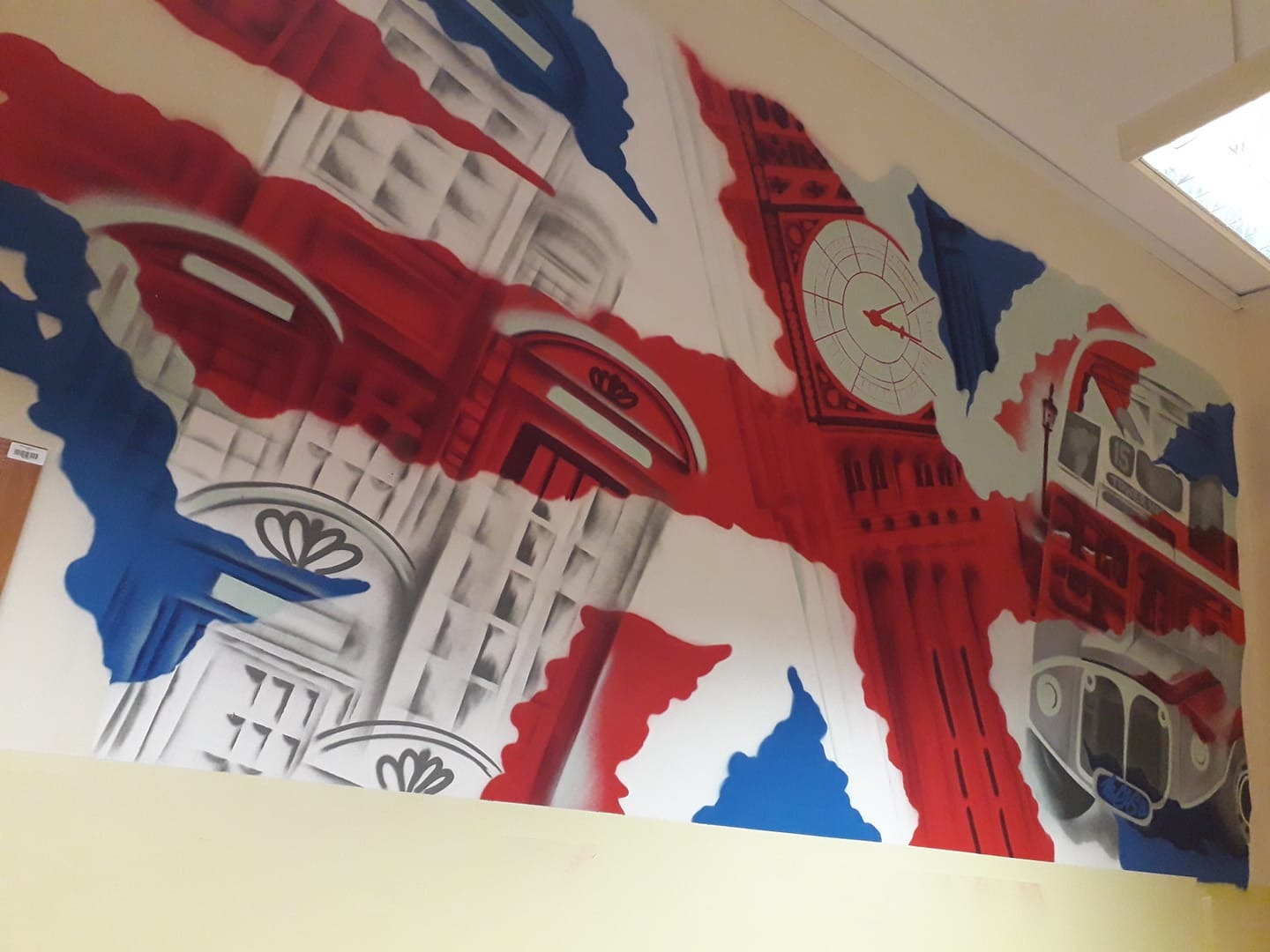 Ścienne malowidło w stylu graffiti przedstawiające motywy Londynu: Big Ben, czerwona budka telefoniczna i autobus, wkomponowane w flagę Wielkiej Brytanii.