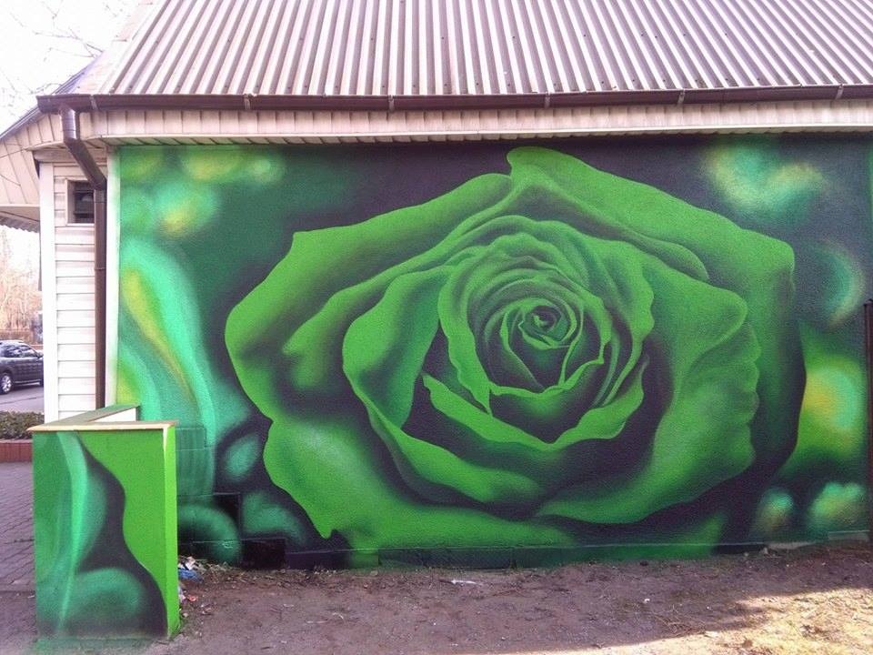 Zielona róża, mural na ścianie budynku, z dopasowanym kolorystycznie śmietnikiem obok.