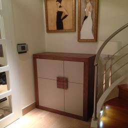 Sławmar Mebel Styl s.c. - Nowoczesna szafka z drewnianymi elementami i kwadratowym uchwytem, umieszczona pod obrazami w eleganckim wnętrzu z drewnianymi schodami.