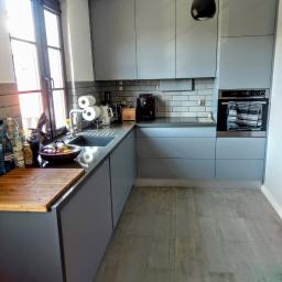 Sławmar Mebel Styl s.c. - Szara kuchnia z drewnianym blatem, ciemnym zlewem i szarą glazurą na ścianie, z widocznym oknem i czarną lampą wiszącą.