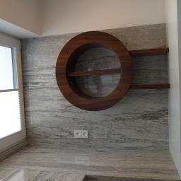 Sławmar Mebel Styl s.c. - Okrągła, drewniana półka z dwoma poziomami wbudowana w kamienną ścianę, obok okno z roletą i fragment szafy.