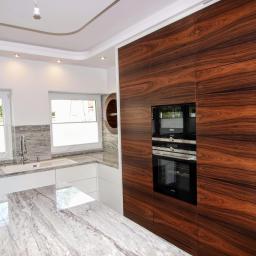Sławmar Mebel Styl s.c. - Nowoczesna kuchnia z wyspą i zabudową z forniru egzotycznego, zintegrowanymi piekarnikami Siemens i blatem z jasnego granitu z wyraźnym użyleniem.