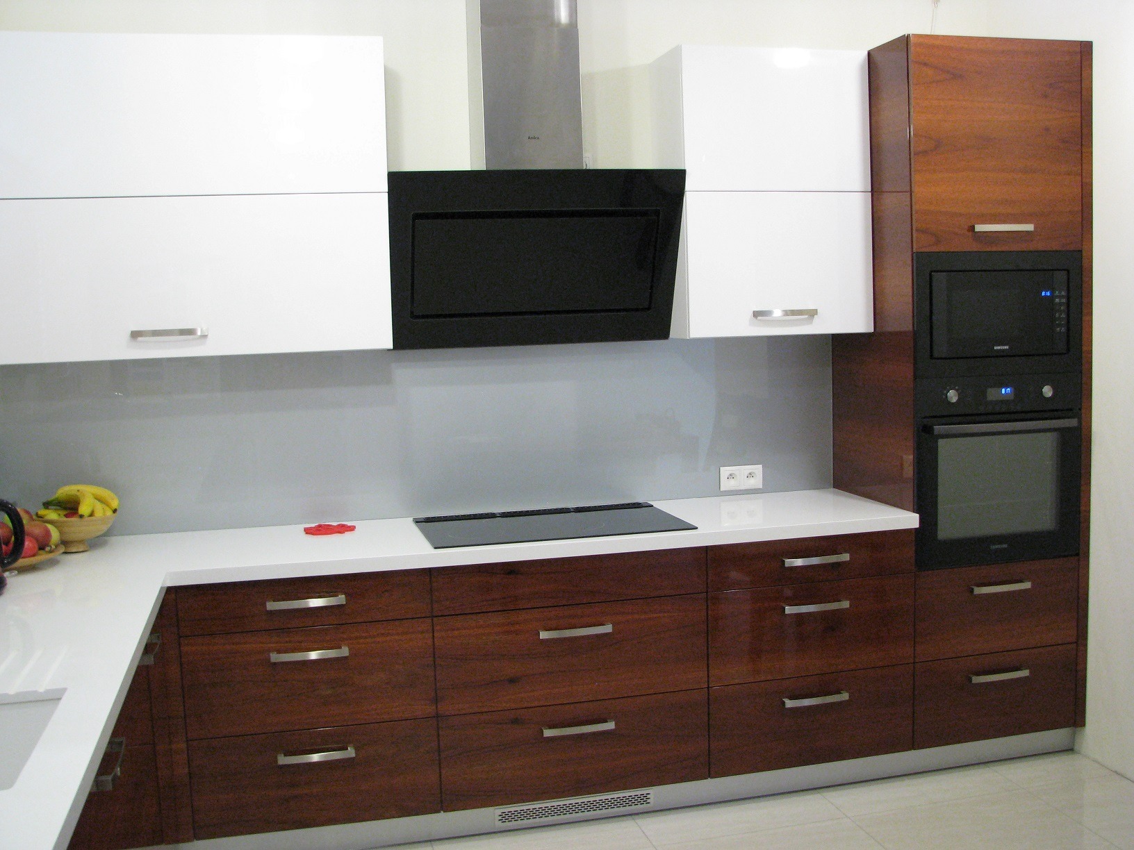 Nowoczesna kuchnia z białymi szafkami górnymi i drewnianymi dolnymi, w zabudowie znajduje się piekarnik i mikrofalówka, a na blacie płyta indukcyjna. Realizacja w Jabłonnie.