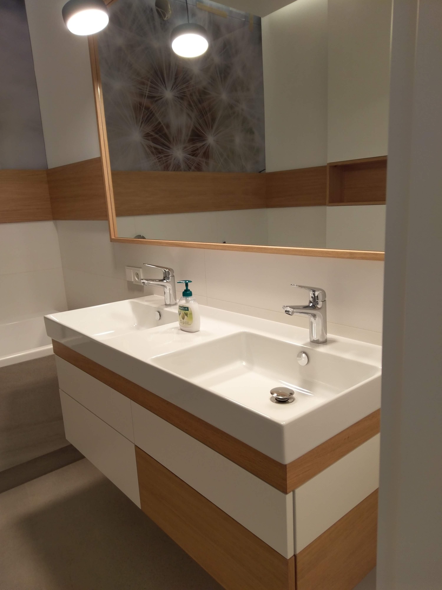 Podwójna umywalka nablatowa z szafką w odcieniach bieli i drewna, chromowana bateria, mydło w płynie, lustro z oświetleniem w nowoczesnej łazience.