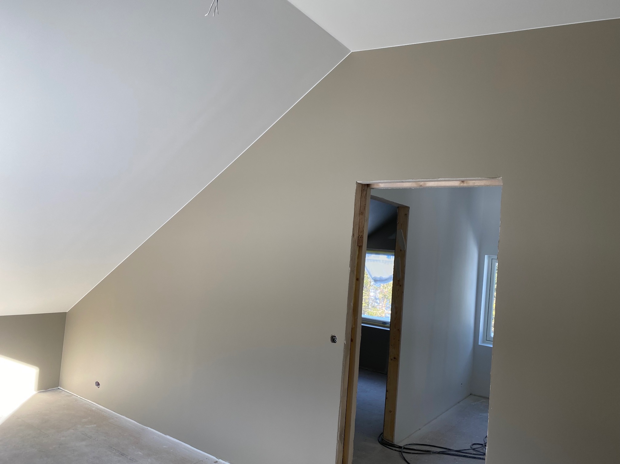 Poddasze po malowaniu: gładkie, beżowe ściany, biały sufit, widoczne kable elektryczne wystające ze ściany, surowe obramowanie drzwi.