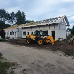 Budowa domu z bloczków betonu komórkowego, widoczna konstrukcja dachu i żółta ładowarka teleskopowa JCB 540.