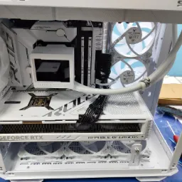 Wnętrze białej obudowy komputera PC z widocznymi komponentami: kartą graficzną GeForce RTX, chłodzeniem procesora, pamięcią RAM Fury i wentylatorami TUF Gaming, wszystko utrzymane w białej...