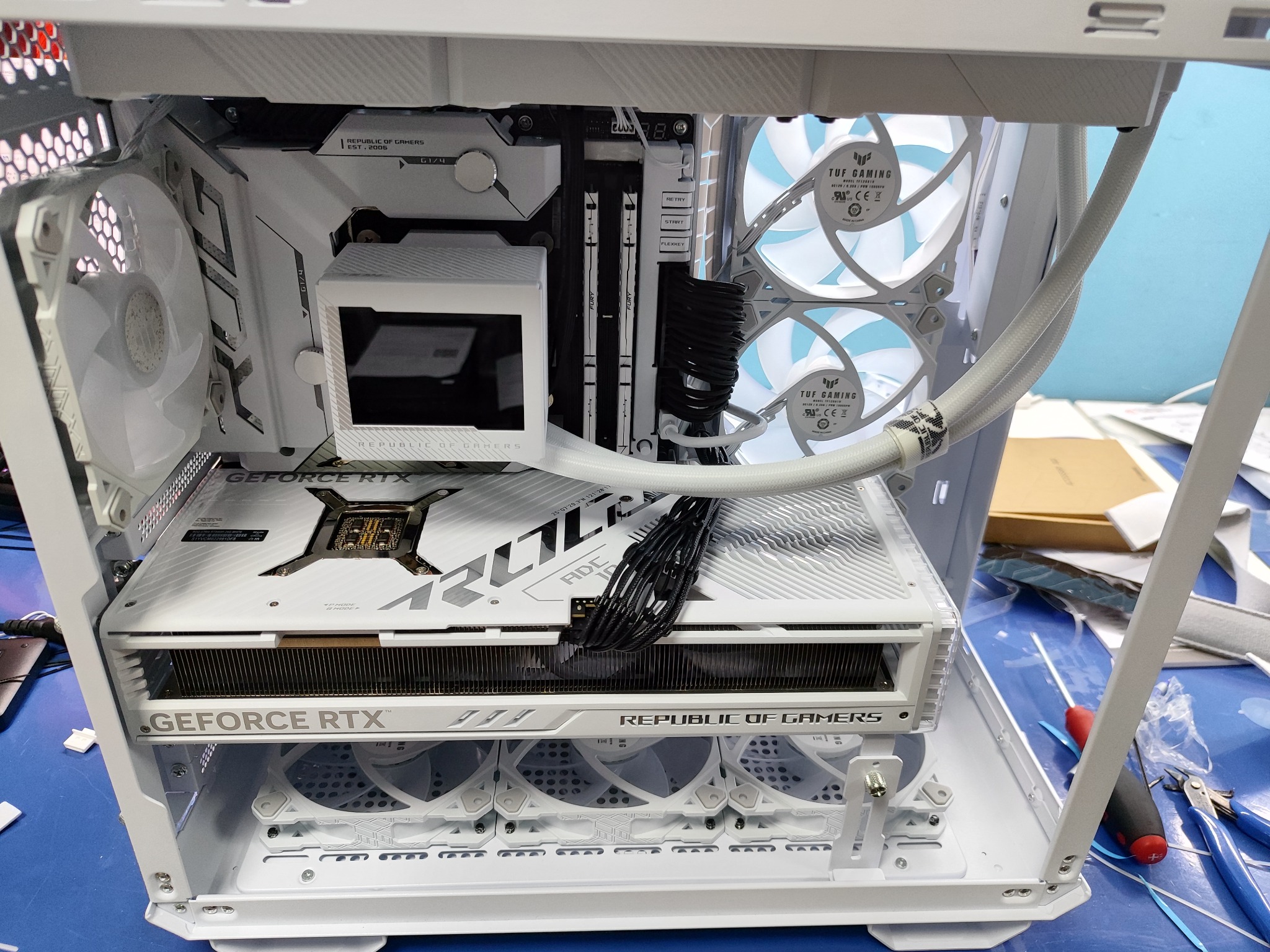 Wnętrze białej obudowy komputera PC z widocznymi komponentami: kartą graficzną GeForce RTX, chłodzeniem procesora, pamięcią RAM Fury i wentylatorami TUF Gaming, wszystko utrzymane w białej...