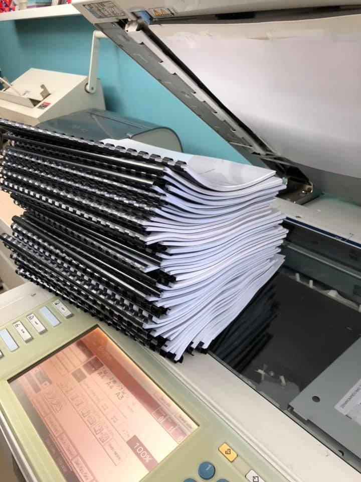 Stos zadrukowanych, zbindowanych dokumentów leżący na urządzeniu wielofunkcyjnym z otwartą klapą skanera.