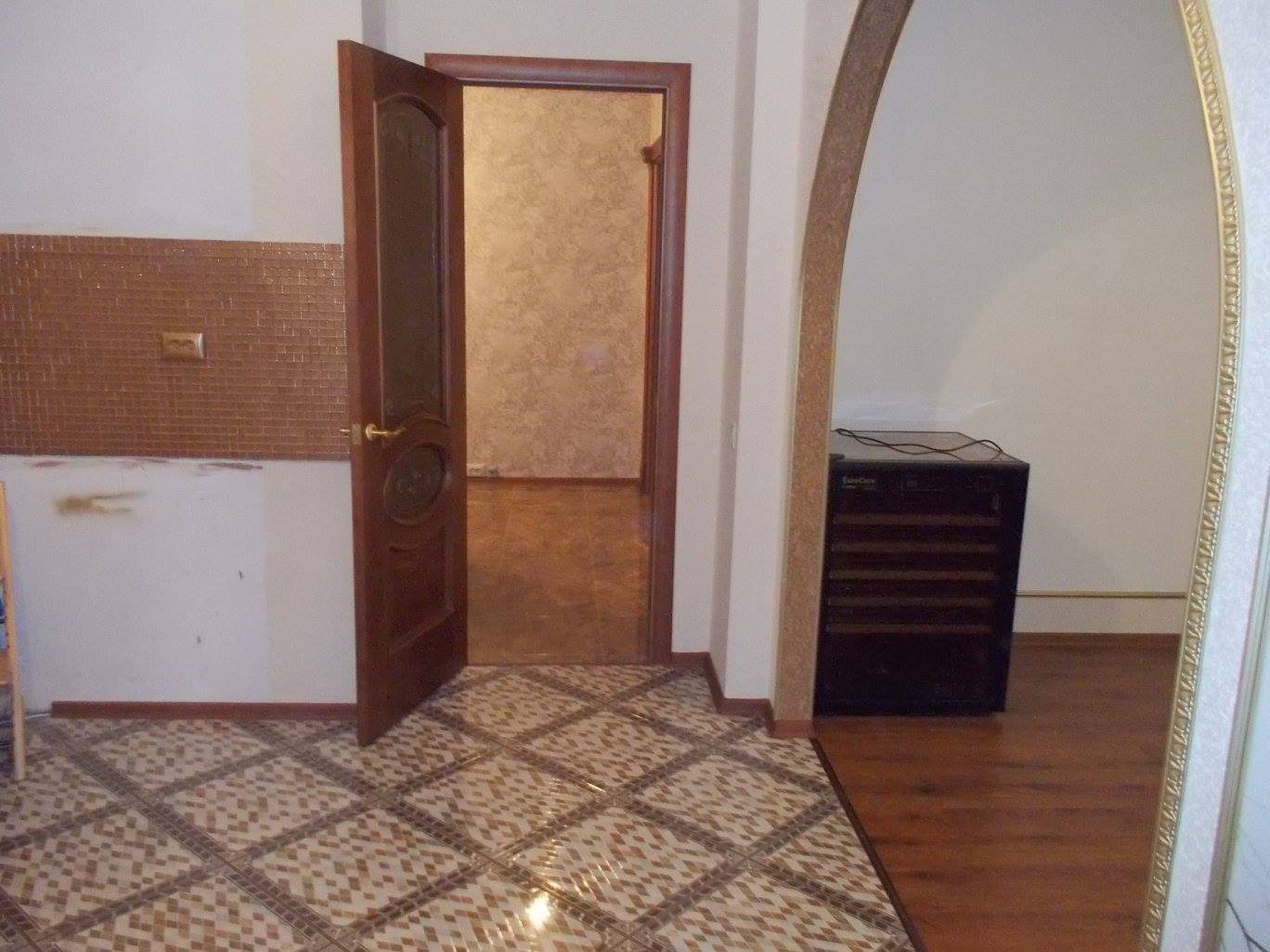 Otwarta drewniana dębowa okleina drzwiowa z szybą w Szczecinie, widoczna mozaika na ścianie i wzorzysta brązowo-beżowa terakota na podłodze.