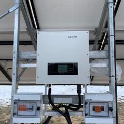 MILTON-PV - Instalacja fotowoltaiczna: inwerter Sofar Solar zamontowany na metalowej konstrukcji, widoczne bezpieczniki w obudowach, częściowo ośnieżone podłoże.
