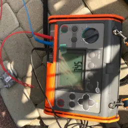 Miernik rezystancji uziemienia Sonel MRU-21 z podłączonymi przewodami pomiarowymi i sondą, leżący na kostce brukowej, wskazujący wartość 7.45 Ω.