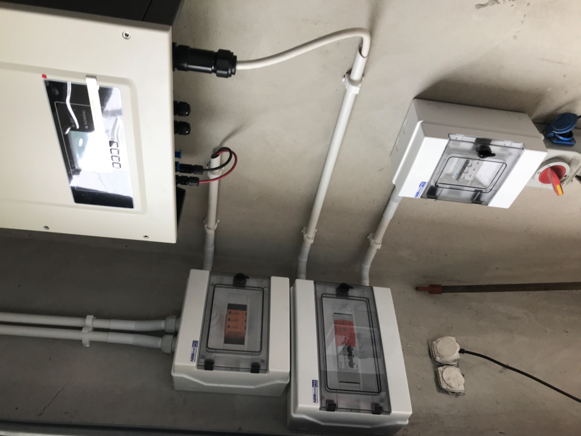 Szare wnętrze z zamontowanym inwerterem, rozdzielnicą i przewodami instalacji elektrycznej.