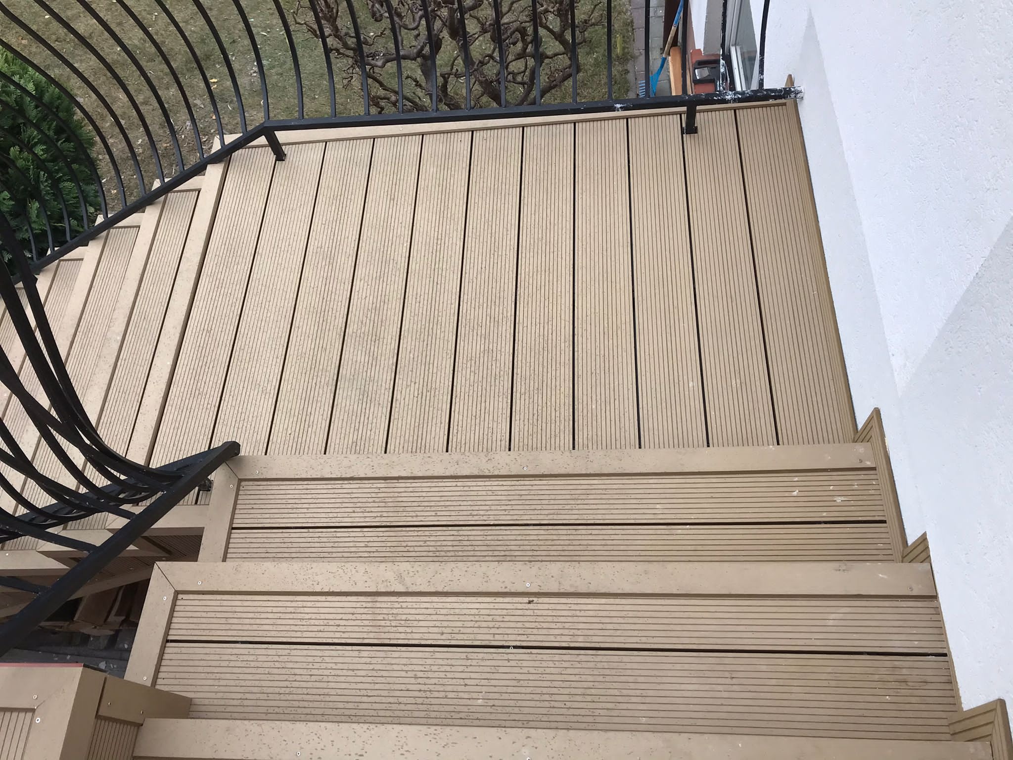 Schody z desek kompozytowych prowadzące na taras z czarną, metalową balustradą.