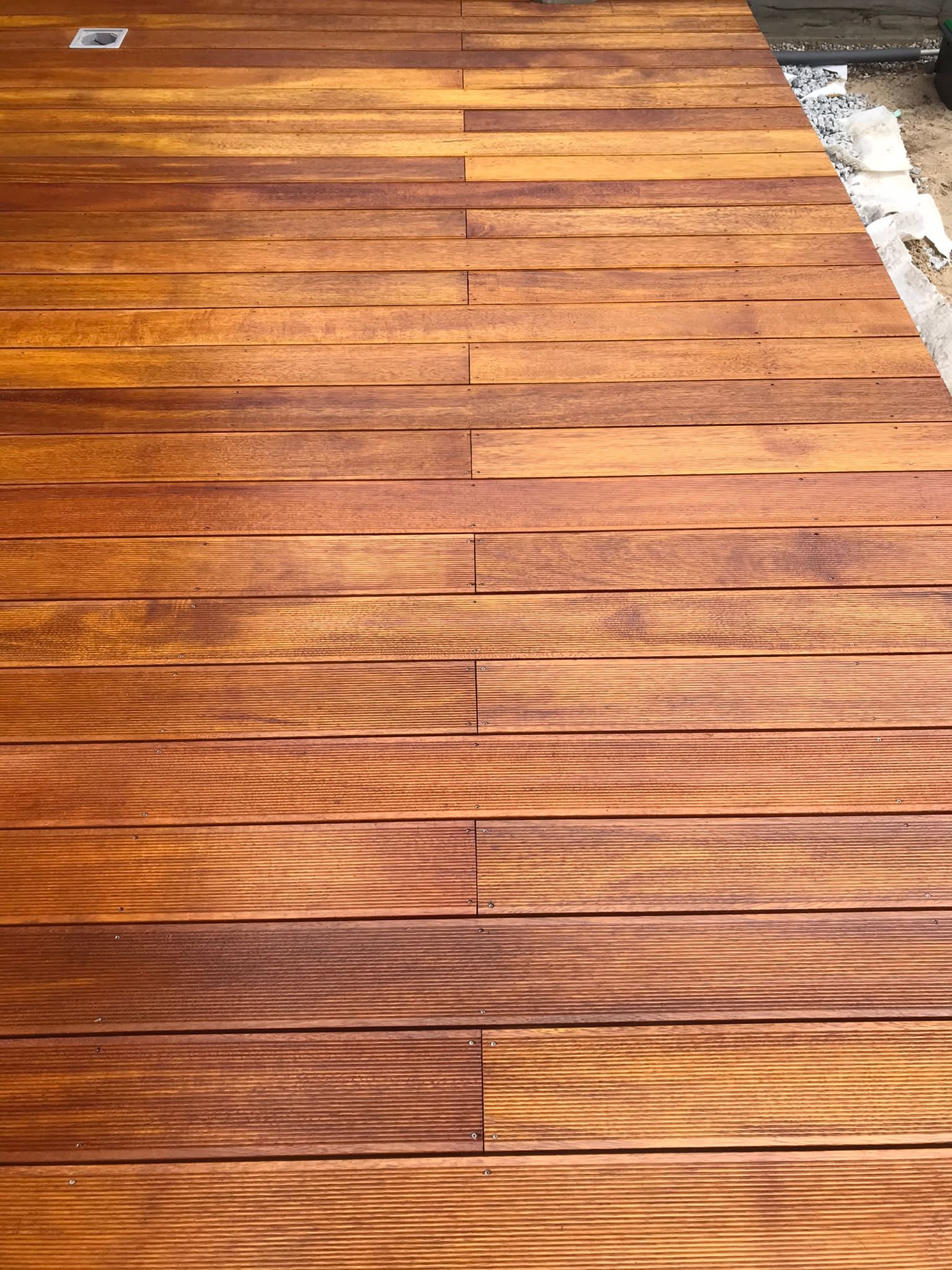 Nowa drewniana podłoga z desek tarasowych o ciepłym, brązowo-pomarańczowym odcieniu, widoczne drobne ślady montażu przy krawędzi.