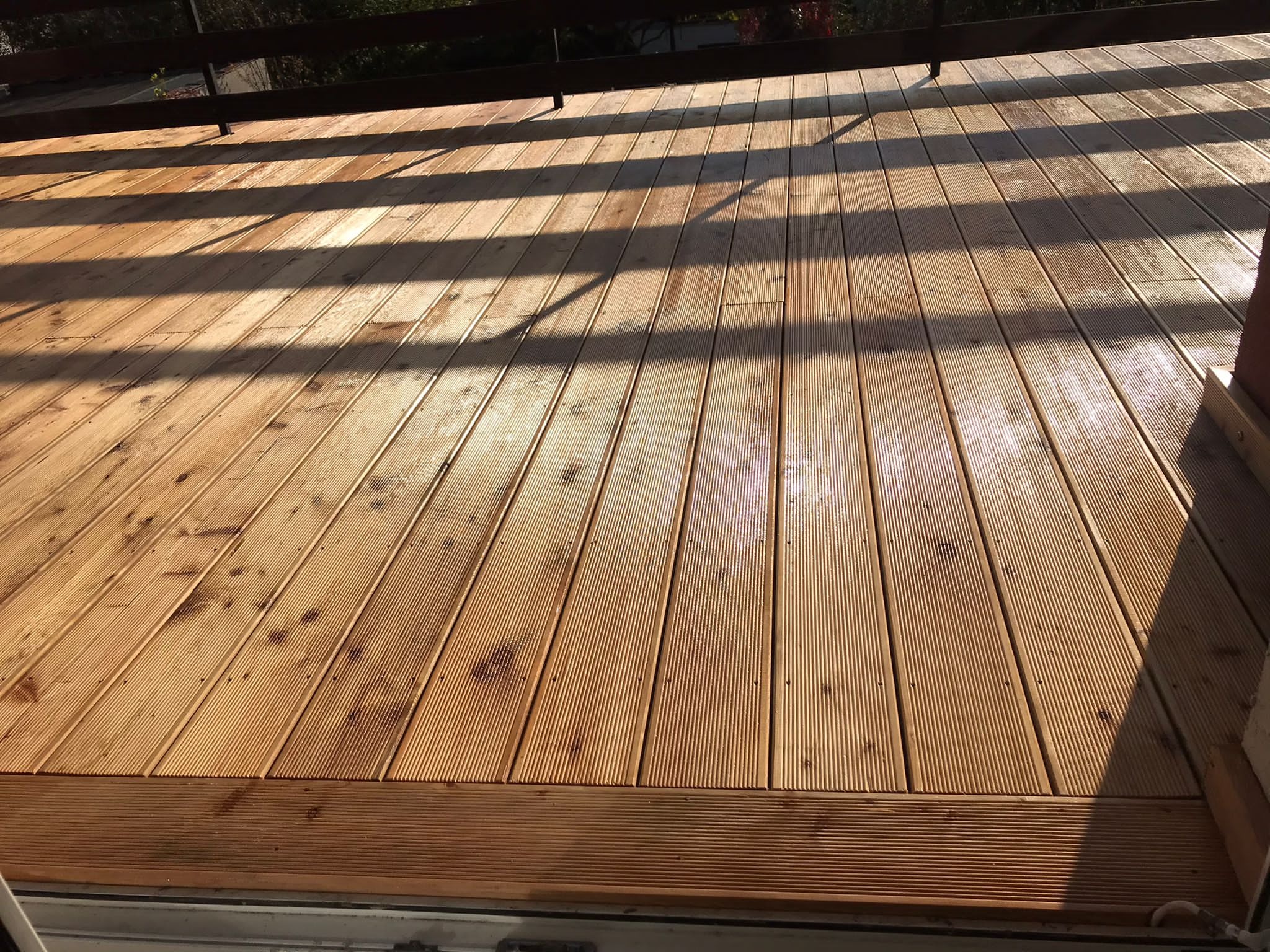 Drewniana podłoga tarasu z widocznymi promieniami słońca i cieniem balustrady, deski ryflowane, jasne drewno.
