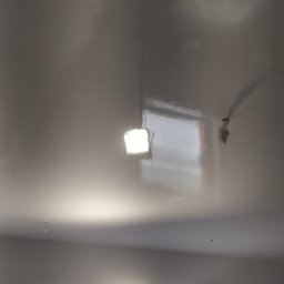 Tomasz Mazur - Świeżo pomalowany sufit z widocznym odbiciem światła lampy halogenowej, okno zabezpieczone folią malarską, widoczne ślady po montażu oświetlenia.