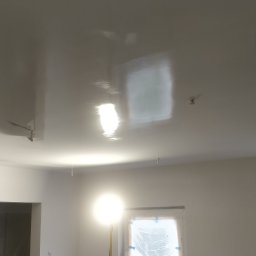 Tomasz Mazur - Świeżo pomalowany, błyszczący sufit w pokoju, zabezpieczone okna folią malarską, widoczne ślady po taśmie malarskiej.