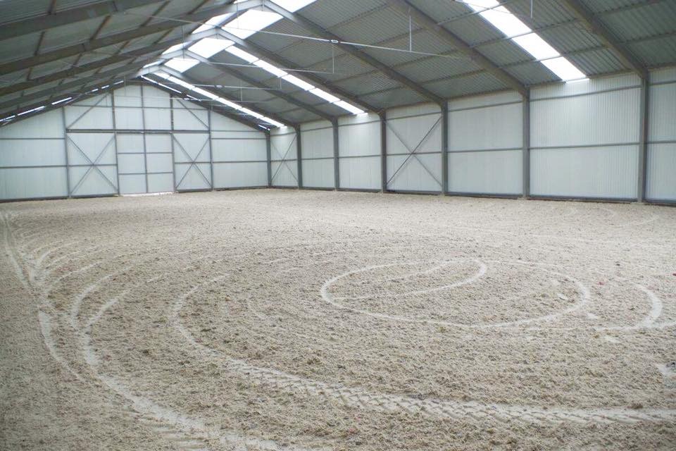 Wnętrze hali z metalową konstrukcją i ścianami z blachy trapezowej, piaszczysta powierzchnia z widocznymi śladami opon i wyrysowanymi okręgami.