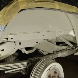 Podwozie samochodu po piaskowaniu i zabezpieczeniu antykorozyjnym, przygotowane do dalszych prac. Widoczne elementy zawieszenia i koła pokryte farbą.