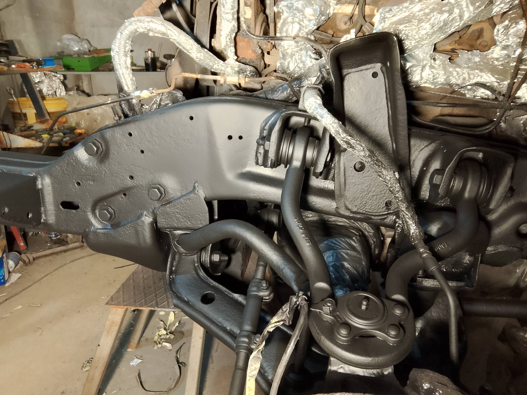 Odnowione podwozie pojazdu z elementami zawieszenia, świeżo pokryte czarną farbą antykorozyjną. Widoczne przewody i elementy owinięte folią.