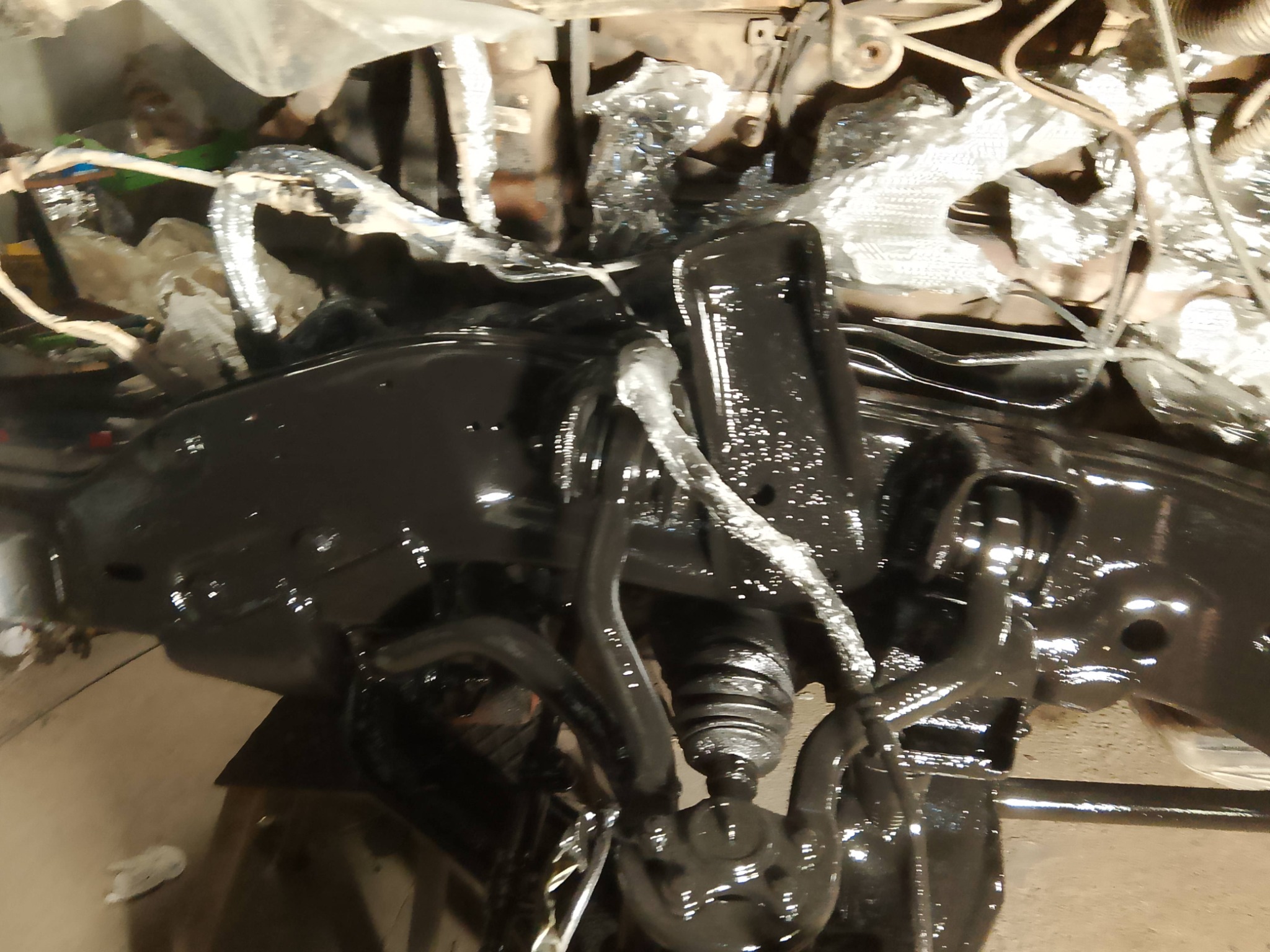 Antykorozyjne zabezpieczenie podwozia samochodu, świeżo po nałożeniu czarnej powłoki ochronnej. Widoczne elementy zawieszenia i osłonięte przewody.